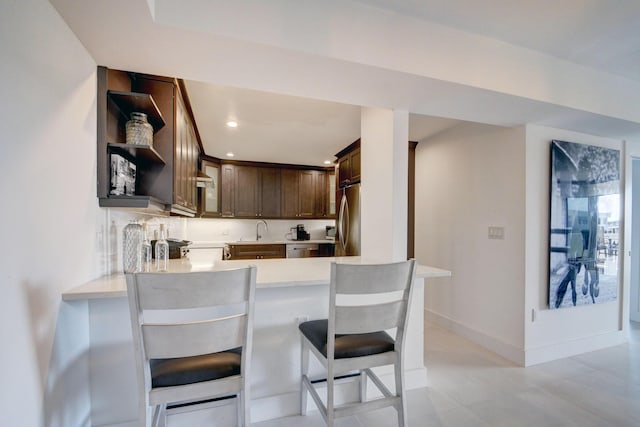 kitchen with dark brown cabinetry, open shelves, appliances with stainless steel finishes, a sink, and light countertops