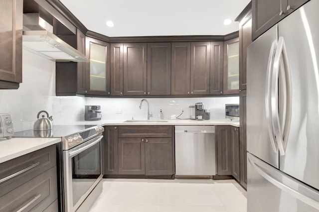 kitchen with a sink, wall chimney range hood, dark brown cabinetry, stainless steel appliances, and decorative backsplash