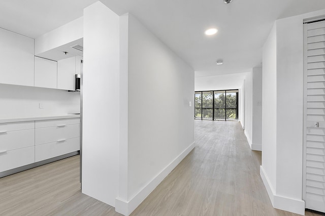 hallway with light wood-style flooring, baseboards, and visible vents