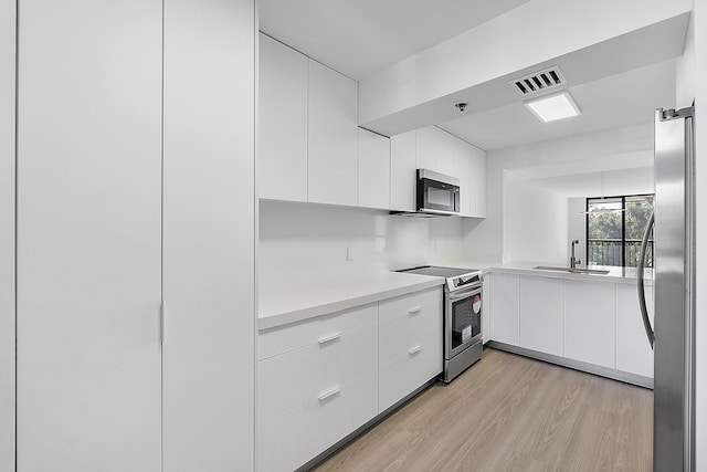 kitchen with modern cabinets, white cabinetry, visible vents, appliances with stainless steel finishes, and a sink