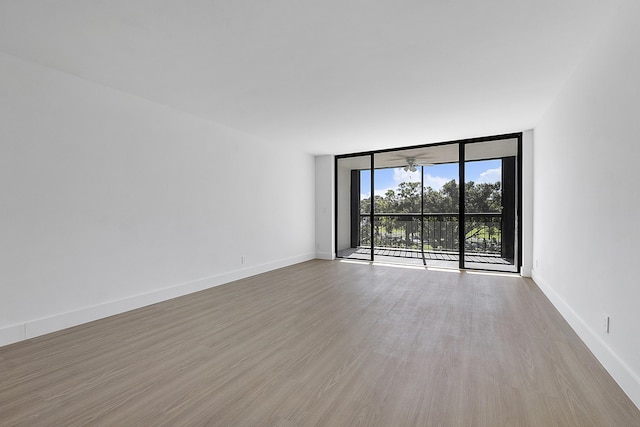 empty room with expansive windows, baseboards, and wood finished floors