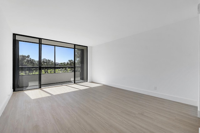 unfurnished room with a wall of windows, wood finished floors, and baseboards