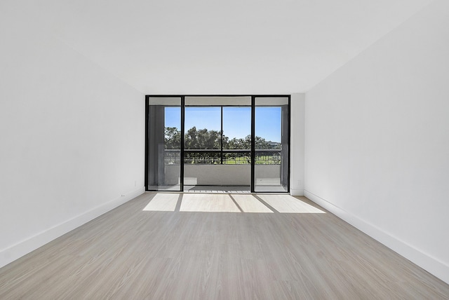 spare room with wood finished floors, floor to ceiling windows, and baseboards