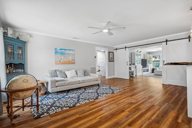 living area featuring ornamental molding, a barn door, and wood finished floors