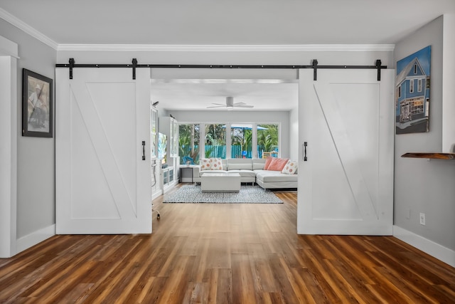 living room featuring baseboards, ornamental molding, a barn door, and wood finished floors