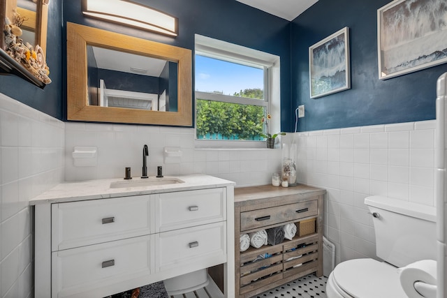 bathroom with tile walls, a wainscoted wall, vanity, and toilet