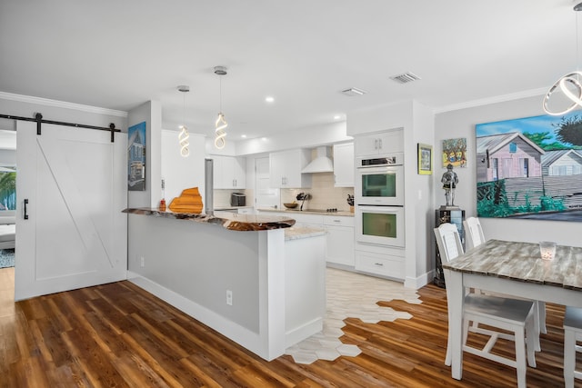 kitchen with crown molding, double oven, wall chimney exhaust hood, and visible vents