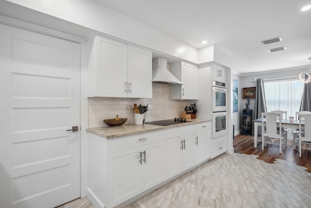 kitchen featuring stainless steel double oven, visible vents, tasteful backsplash, premium range hood, and white cabinets
