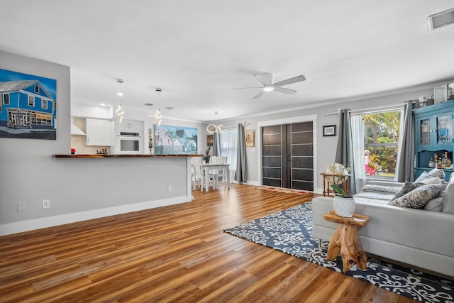 living room featuring visible vents, crown molding, wood finished floors, baseboards, and a ceiling fan