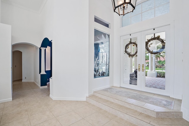 tiled foyer with french doors, arched walkways, a high ceiling, and baseboards