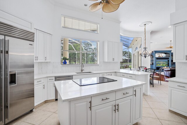 kitchen with ceiling fan with notable chandelier, light tile patterned floors, a center island, a sink, and stainless steel appliances