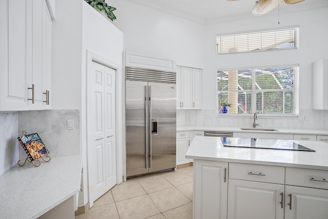 kitchen featuring light tile patterned floors, ornamental molding, white cabinetry, black electric cooktop, and stainless steel built in fridge