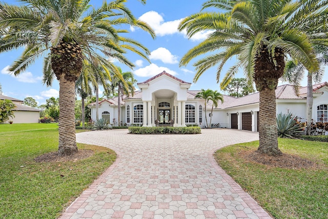 mediterranean / spanish home featuring a front yard, a tiled roof, an attached garage, stucco siding, and curved driveway