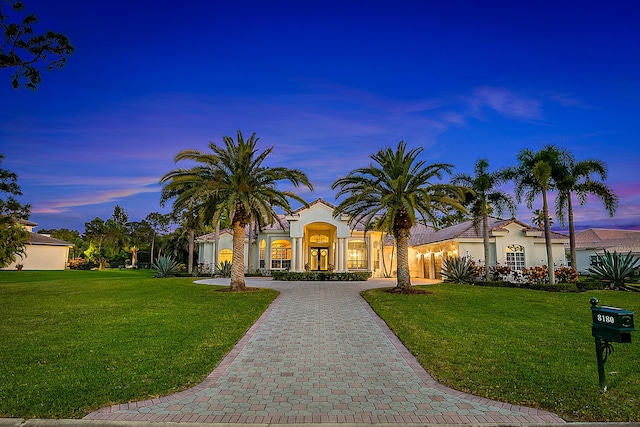 mediterranean / spanish home with a yard, stucco siding, and curved driveway