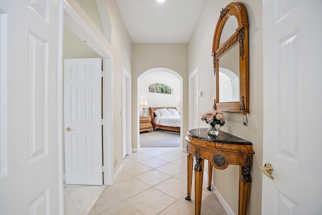 corridor featuring arched walkways, baseboards, and light tile patterned flooring