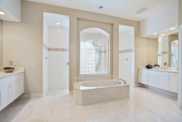 bathroom featuring visible vents, a bath, baseboards, a walk in shower, and two vanities
