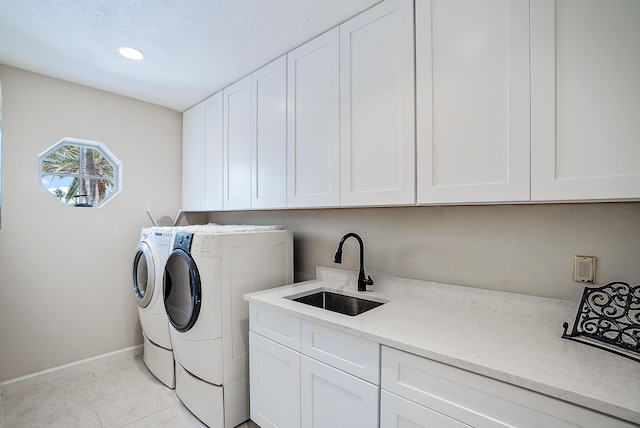 washroom with baseboards, light tile patterned flooring, washer and clothes dryer, cabinet space, and a sink