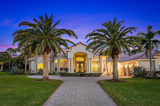 mediterranean / spanish house featuring a yard, stucco siding, a tiled roof, and curved driveway