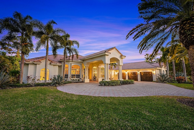 mediterranean / spanish home with a tiled roof, a yard, a garage, and stucco siding