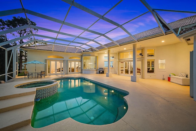 pool at dusk featuring a pool with connected hot tub, french doors, a ceiling fan, and a patio