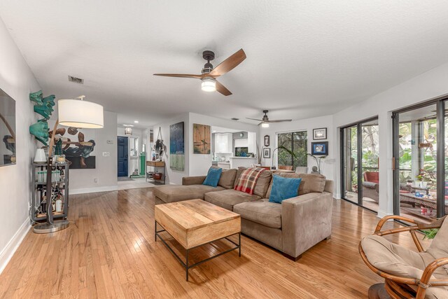 living area featuring a ceiling fan, visible vents, baseboards, and light wood-type flooring