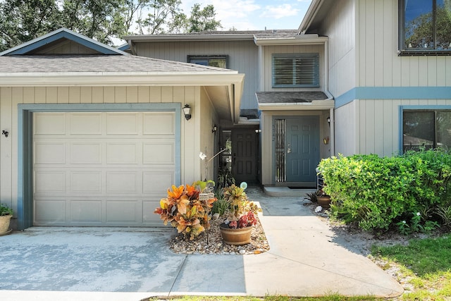 doorway to property with roof with shingles, concrete driveway, and a garage