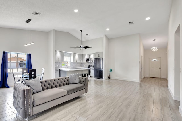 living room with high vaulted ceiling, plenty of natural light, a ceiling fan, light wood-style floors, and baseboards