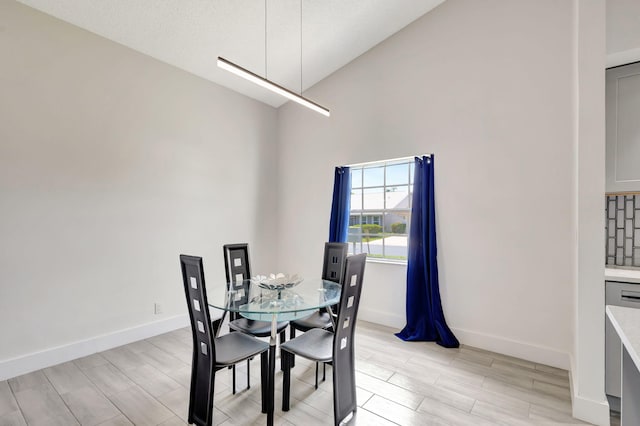 dining room featuring high vaulted ceiling, light wood-style floors, and baseboards
