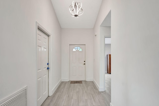 doorway featuring a chandelier, baseboards, and light wood-style floors