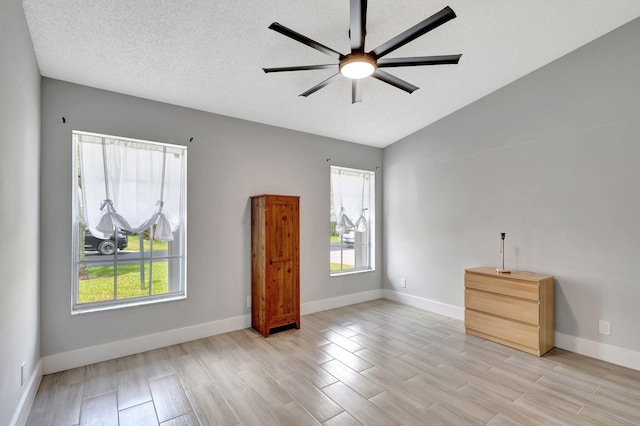 spare room with healthy amount of natural light, ceiling fan, light wood-style floors, baseboards, and lofted ceiling