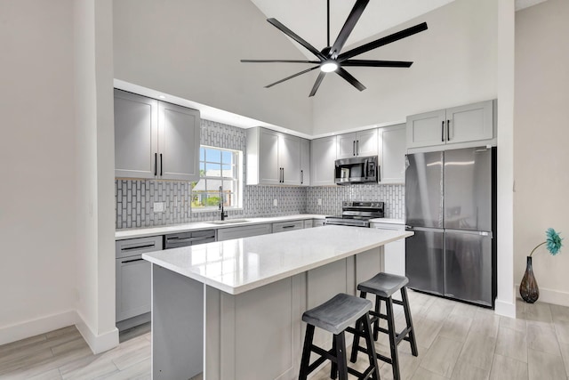 kitchen featuring stainless steel appliances, gray cabinetry, a sink, baseboards, and high vaulted ceiling