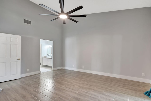 unfurnished room featuring a towering ceiling, light wood-type flooring, ceiling fan, and baseboards