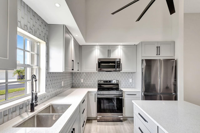 kitchen with appliances with stainless steel finishes, a sink, gray cabinetry, light stone countertops, and recessed lighting