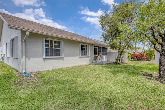back of property with stucco siding, a lawn, and a sunroom