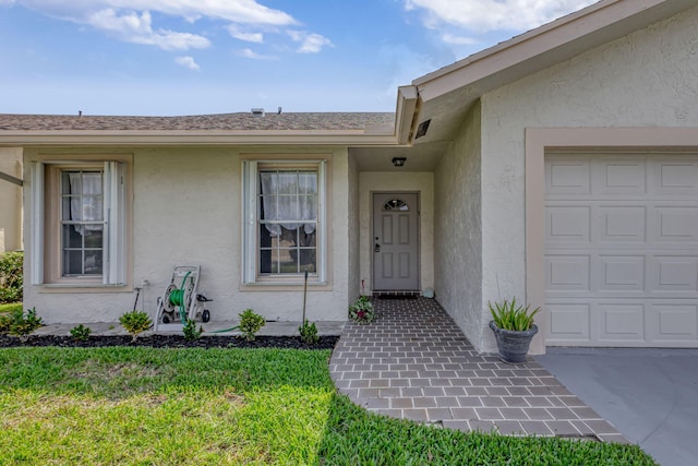 entrance to property featuring stucco siding, a garage, and a lawn