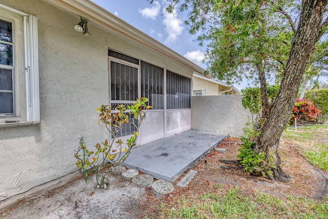 view of property exterior featuring stucco siding, fence, and a sunroom