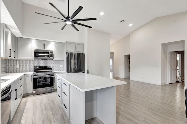 kitchen featuring appliances with stainless steel finishes, decorative backsplash, light countertops, a center island, and high vaulted ceiling