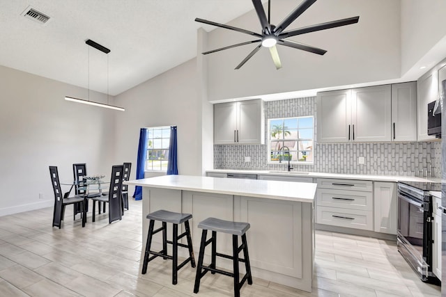 kitchen with stainless steel range with electric cooktop, a sink, decorative backsplash, a ceiling fan, and gray cabinets