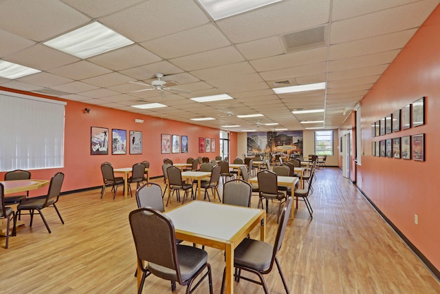 dining space with light wood finished floors, a drop ceiling, baseboards, and ceiling fan
