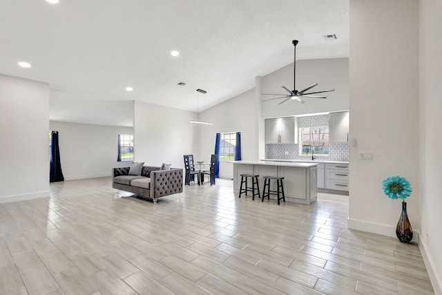 living area featuring plenty of natural light, a ceiling fan, baseboards, recessed lighting, and high vaulted ceiling