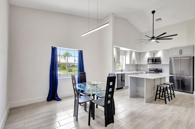 dining space featuring high vaulted ceiling, a ceiling fan, light wood finished floors, and baseboards