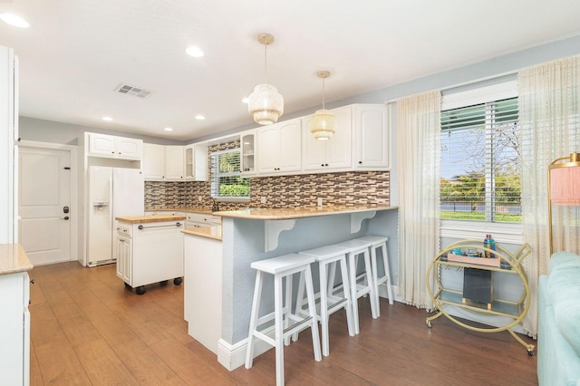 kitchen with white cabinets, white fridge with ice dispenser, a peninsula, dark wood finished floors, and backsplash