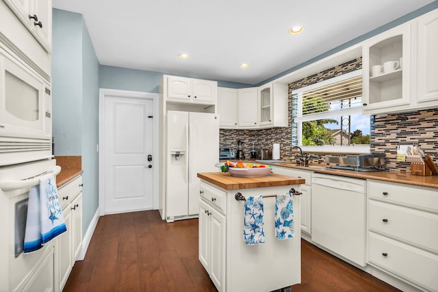 kitchen featuring wooden counters, backsplash, stainless steel microwave, glass insert cabinets, and white cabinetry