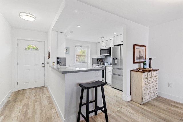 kitchen with light wood finished floors, a peninsula, white cabinetry, and stainless steel appliances