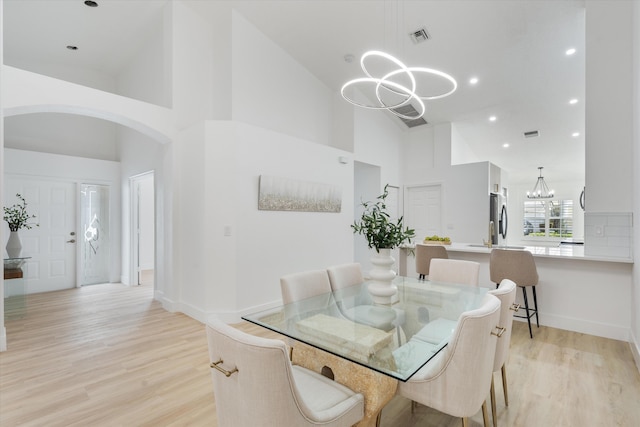 dining space with an inviting chandelier, light wood finished floors, arched walkways, baseboards, and a towering ceiling