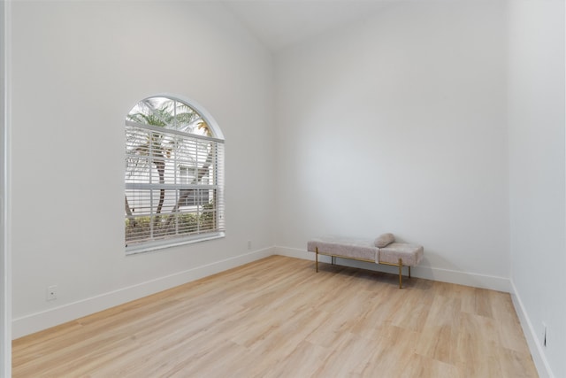 unfurnished room featuring baseboards, lofted ceiling, wood finished floors, and a wealth of natural light