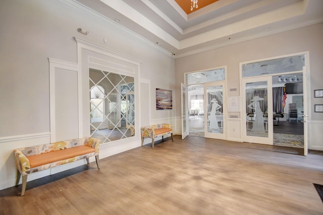 interior space featuring crown molding, a towering ceiling, wood finished floors, a tray ceiling, and french doors