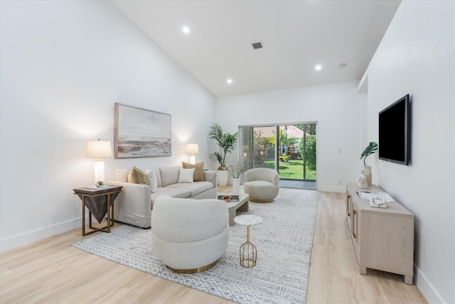 living room with visible vents, light wood-style floors, baseboards, and high vaulted ceiling