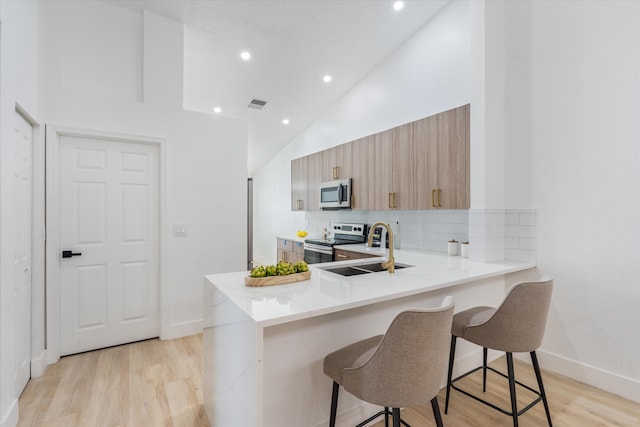 kitchen with visible vents, decorative backsplash, a peninsula, a kitchen bar, and appliances with stainless steel finishes