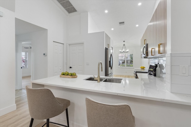 kitchen with visible vents, a sink, a peninsula, light wood-style floors, and stainless steel appliances